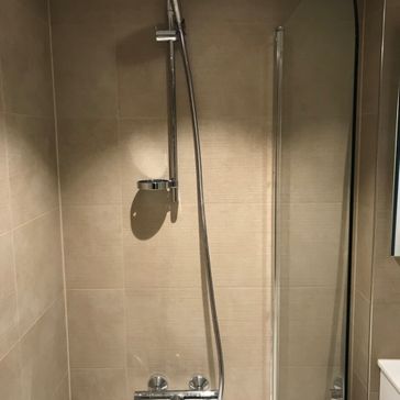 Detaljbillde av dusj som er kombinert med badekar og har en glassvegg som hindrer sprut 