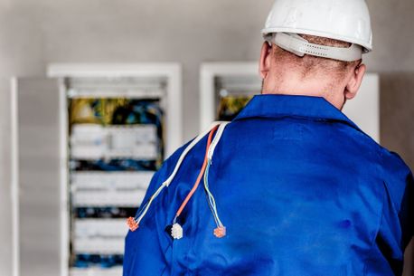 Elektriker i blå uniform og hvit beskyttelseshatt, og har tre ledninger hengende over skuldrene