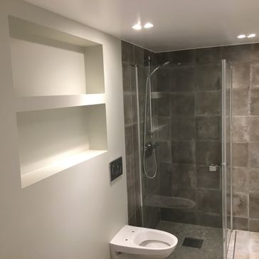Toalett og dusj side om side med dusj innerst i hjørnet og en glassvegg som skiller