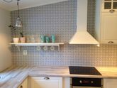 Lyst kjøkken med flislagt mønster på vegg og hylle med kopper og planter