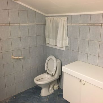 Gammel bad med utdatert toalett og stellebenk og lyseblå fliser