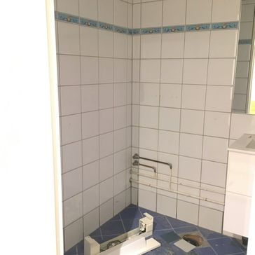 Bad med mørkeblå fliser på gulv og hvite fliser på vegg som blir demontert