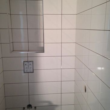Hjørne av bad med oppsett for toalett og hvite fliser på vegg