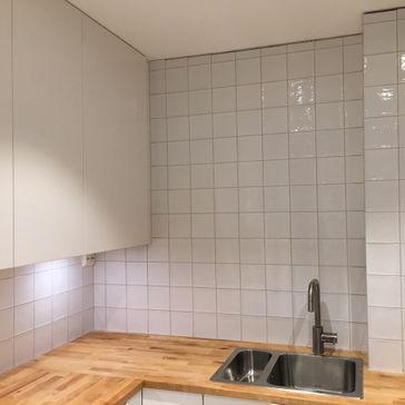 Oppusset kjøkken med stilige hvite fliser på vegg og benkeplate av tre